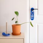 Blauwe deurhanger met het woord chill hangend aan binnendeur naast een dressoir met plant en kandelaar.