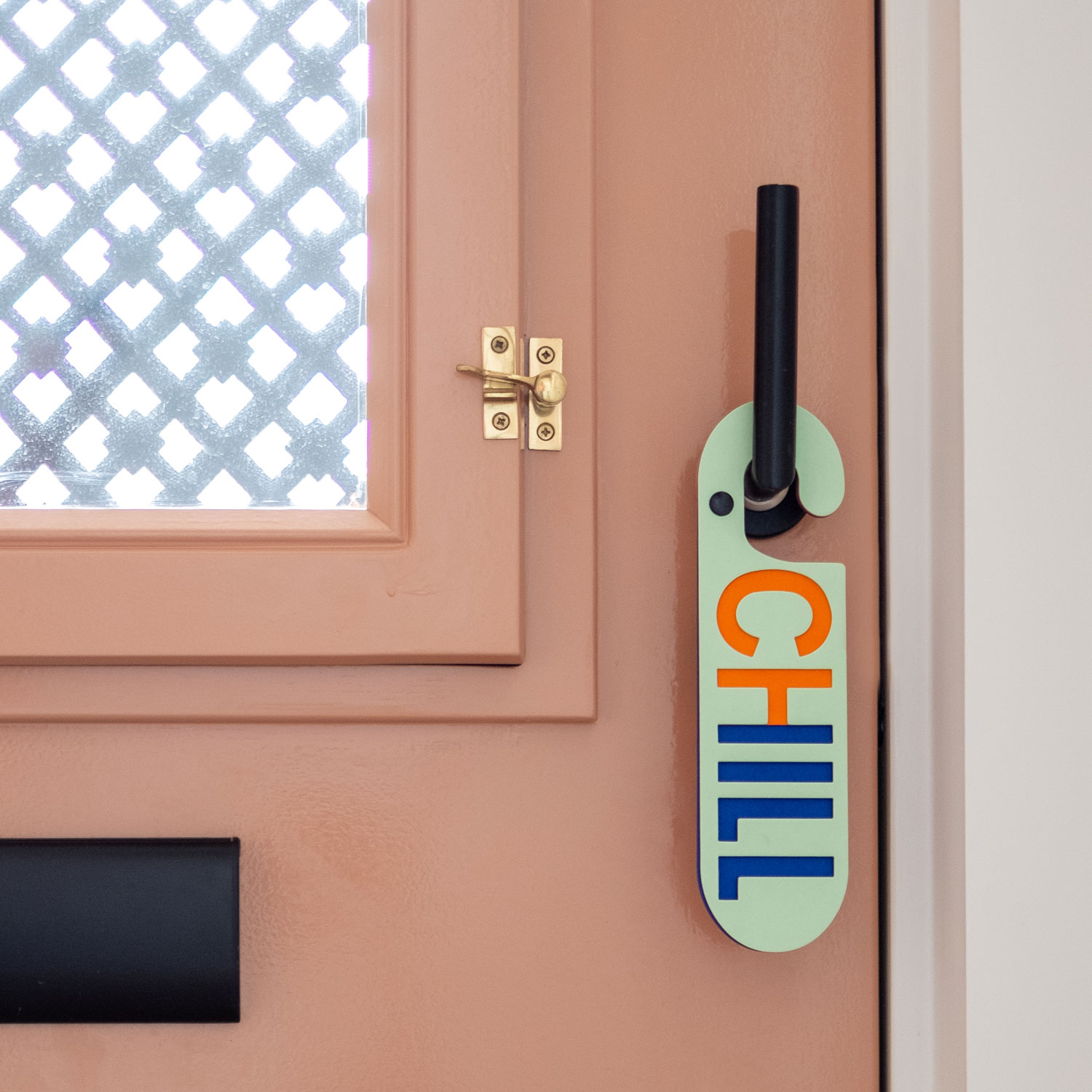 Terracotta kleurige voordeur met licht groene deurhanger met het woord chill