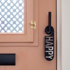 Terracotta kleurige voordeur met zwarte deurhanger met het woord happy