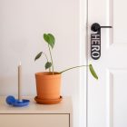 Zwarte deurhanger met het woord hero hangend aan binnendeur naast een dressoir met plant en kandelaar.