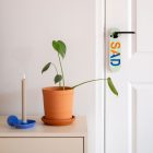 Lichtgroene deurhanger met het woord sad en happy hangend aan binnendeur naast een dressoir met plant en kandelaar.