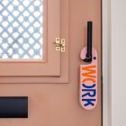 Terracotta kleurige voordeur met roze deurhanger met het woord work