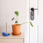 Zwarte deurhanger met het woord work hangend aan binnendeur naast een dressoir met plant en kandelaar.