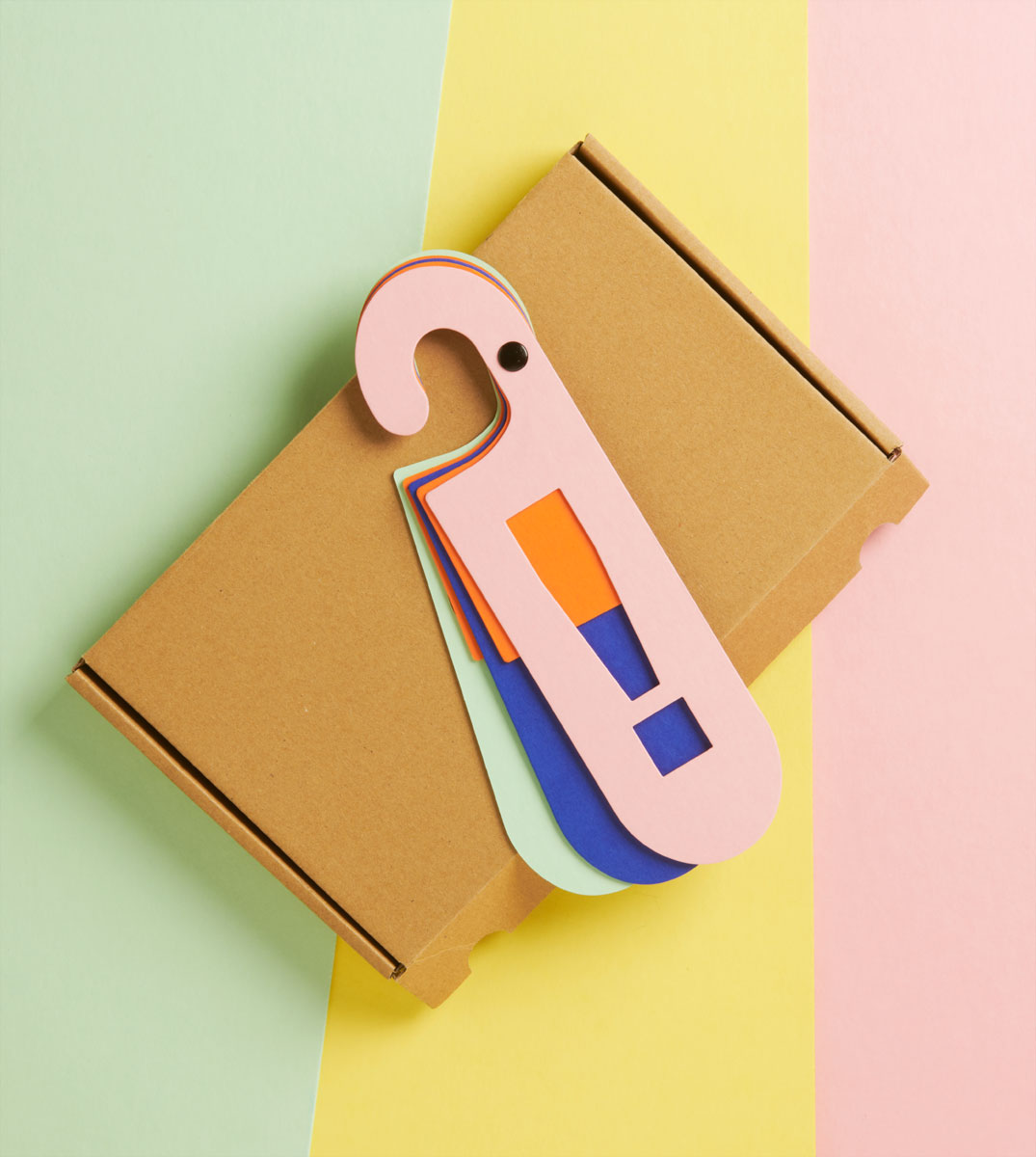 Roze kartonnen deurhanger met een uitroepteken in oranje en blauw.